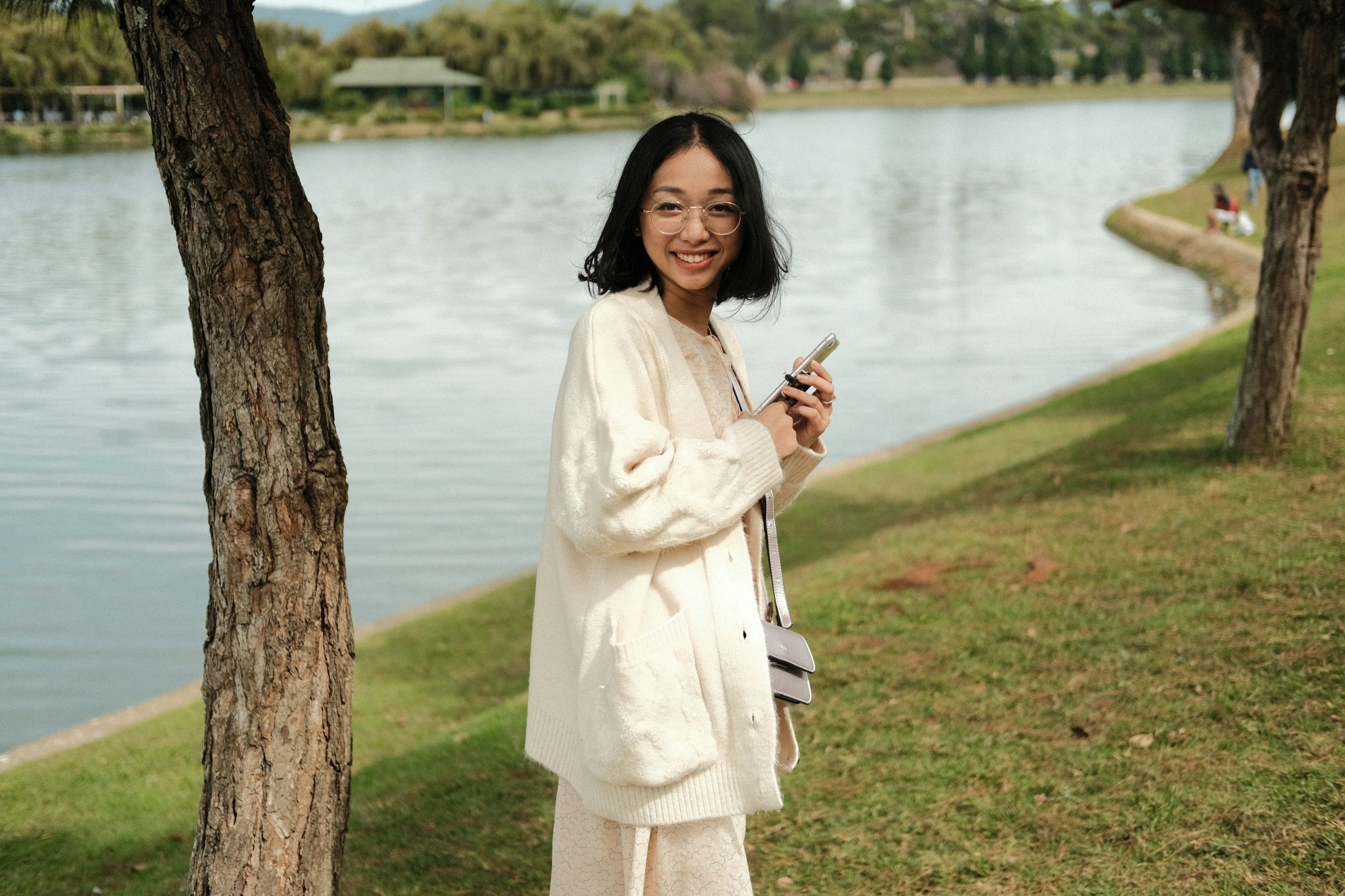 Mujer en vestido blanco de manga larga de pie junto al árbol durante el día