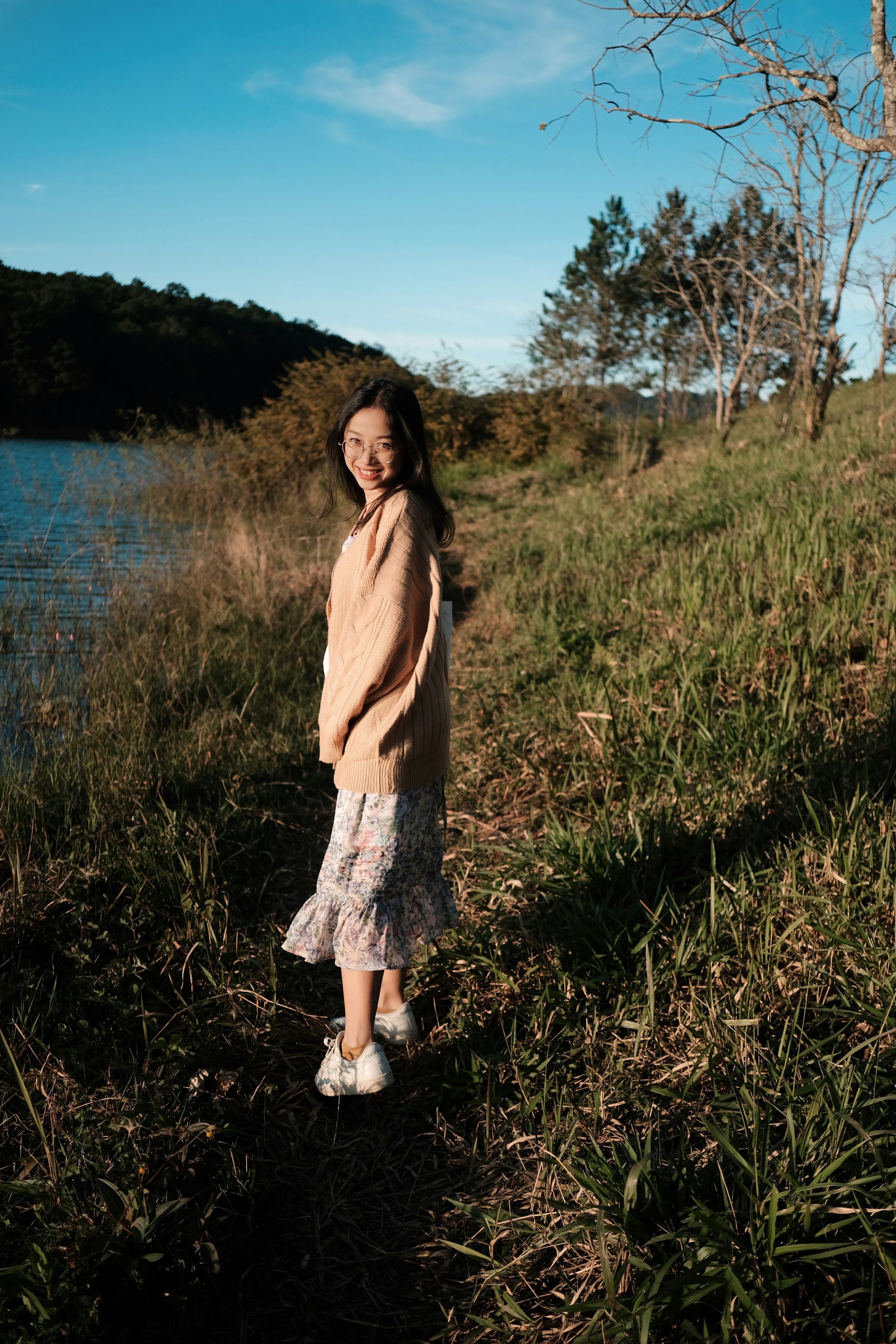 Una niña parada en un campo junto a un cuerpo de agua