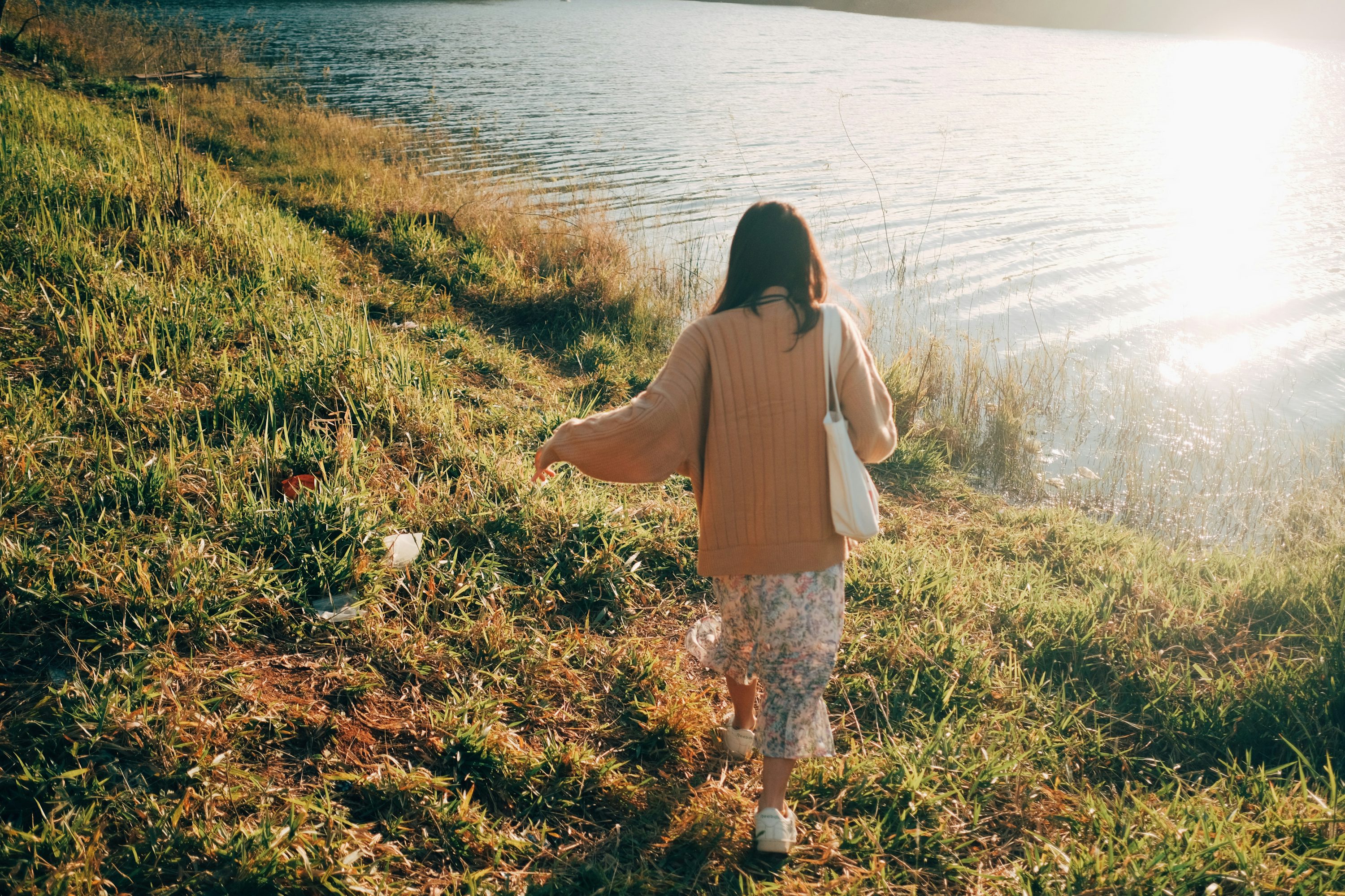 a woman walking along a grass covered hillside next to a body of water