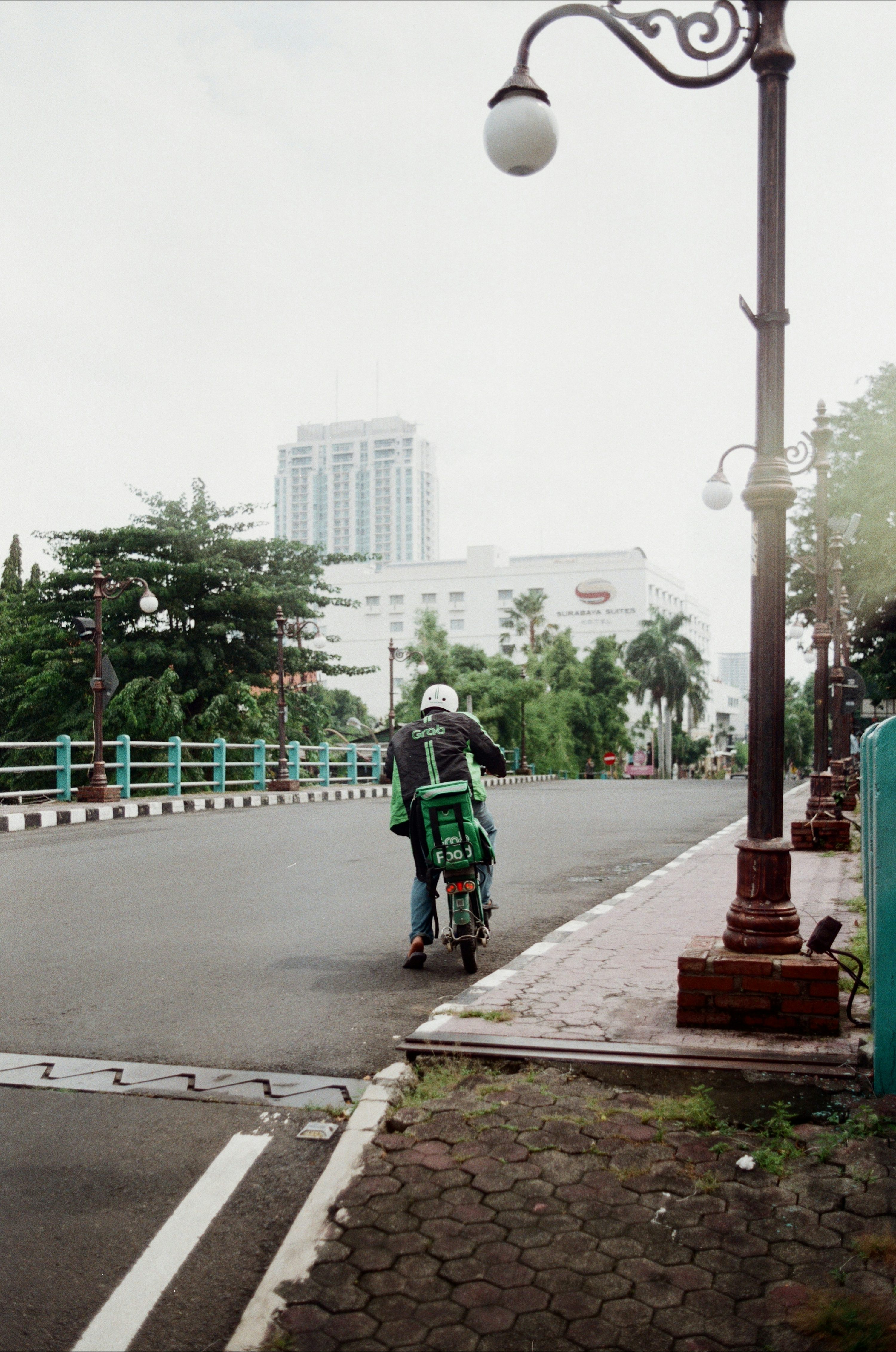 Un hombre conduciendo una motocicleta por una calle junto a un poste de luz