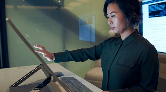 Profilo laterale di una donna che indossa una maglietta scura in un ufficio, mentre scorre con il mouse o lavora su un Surface Studio Microsoft.