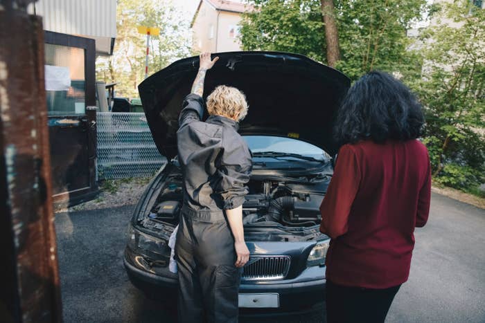 Two people standing by an open car hood, one looking at the engine