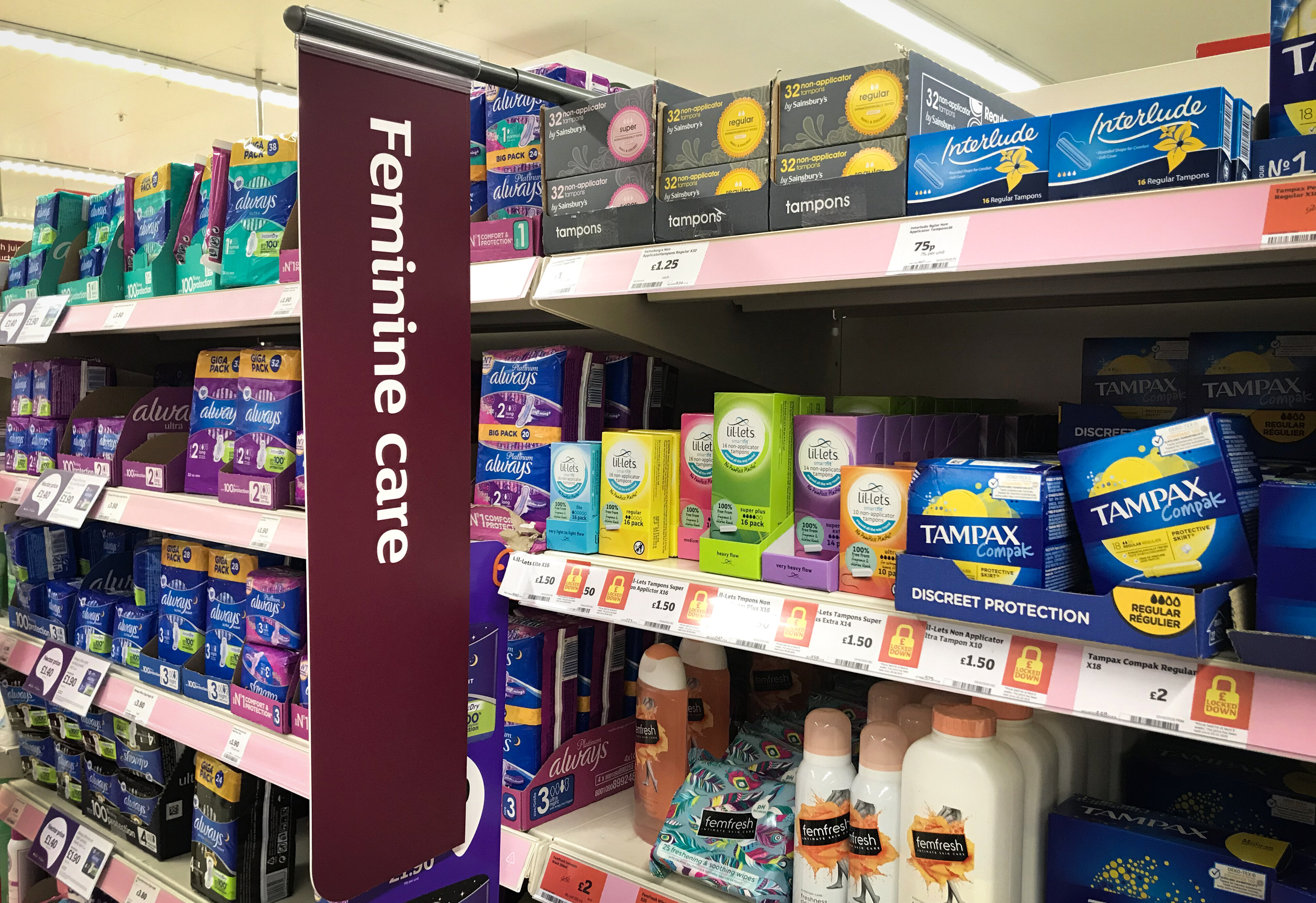 A supermarket aisle filled with various feminine care products such as tampons, pads, and sanitary napkins, with a sign labeled &quot;Feminine care.&quot;