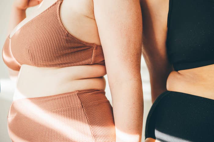 Two people standing back-to-back wearing sports bras and athletic pants, showing body diversity and fitness attire