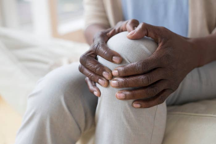 Close-up of a person holding their knee with both hands, appearing to be in pain or discomfort