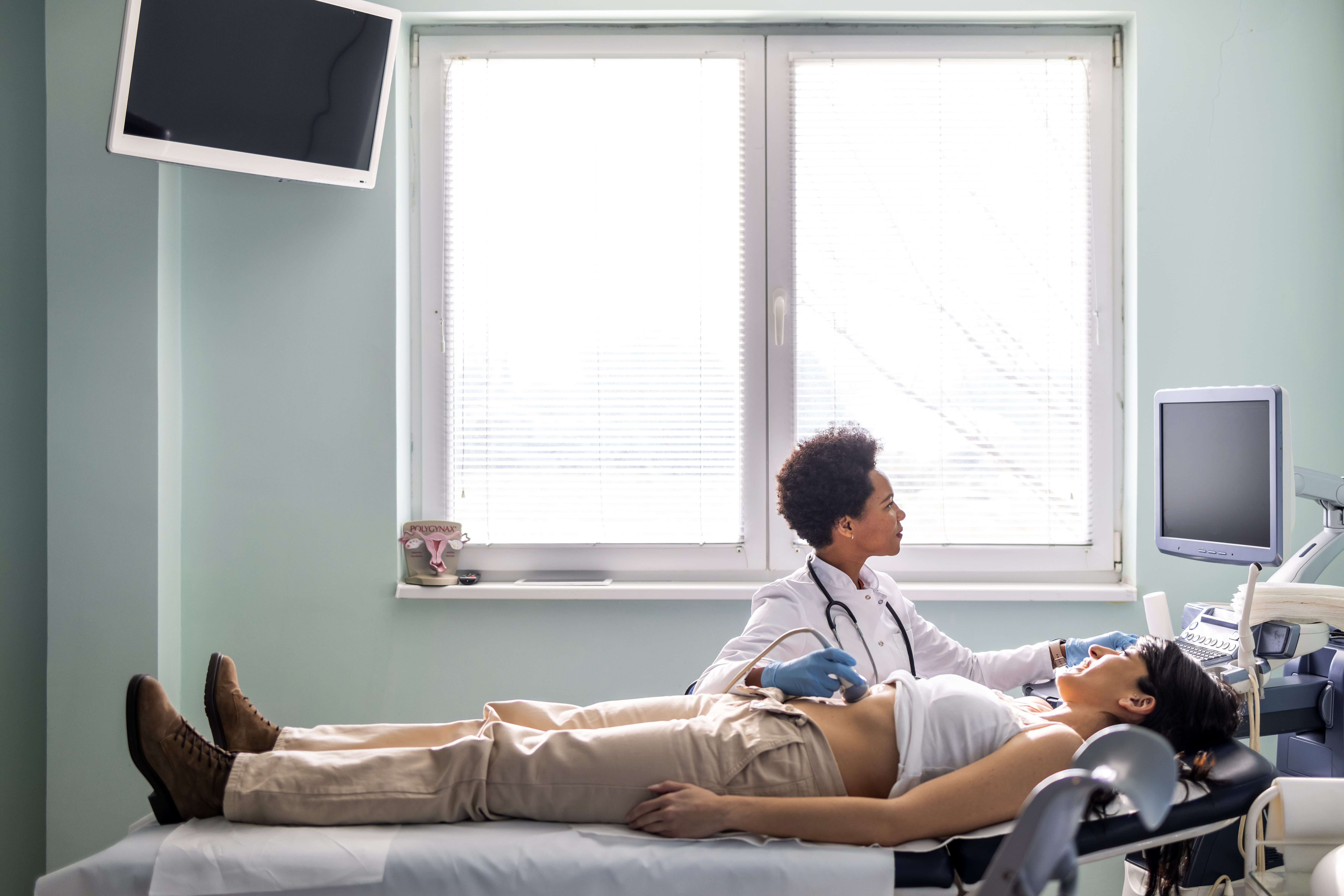 A doctor performs an ultrasound on a patient lying on an examination table in a medical room