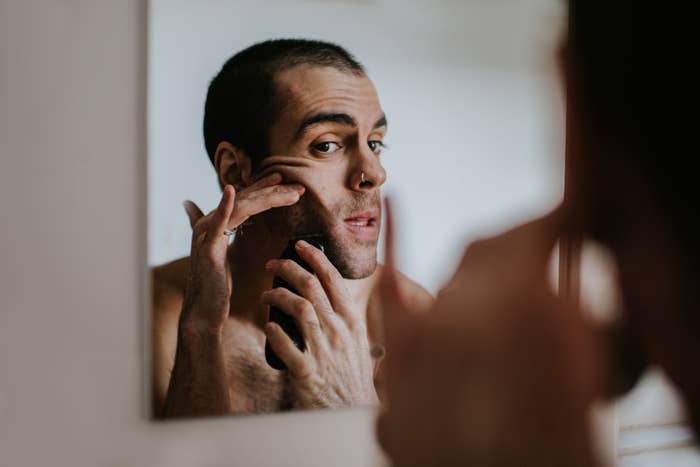 A man is looking into a mirror while shaving his face with an electric razor