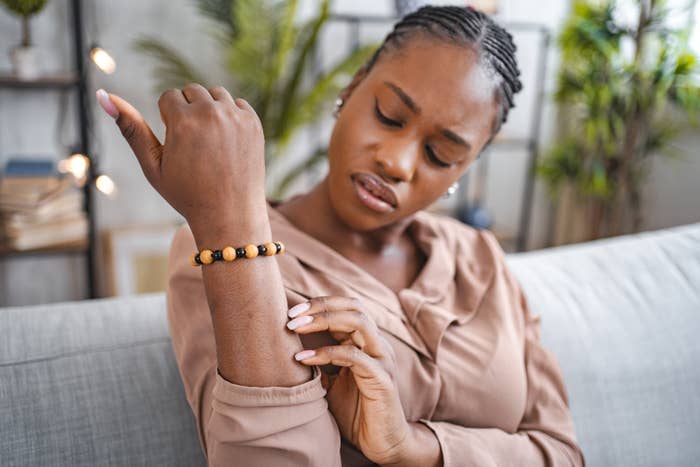 A woman in a blouse examines her right elbow while sitting on a couch