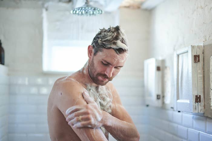 A man showers, washing his hair and body, with soap suds covering his head and arms