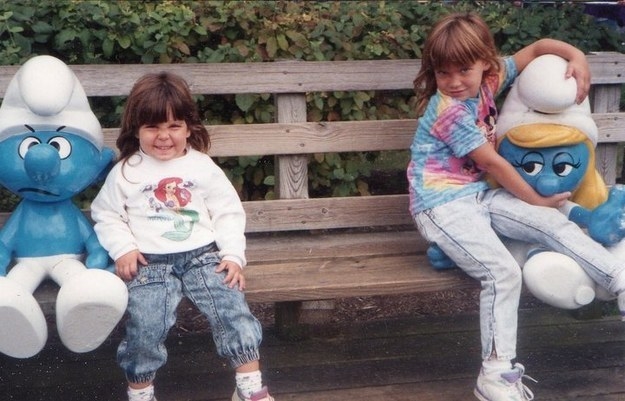 Two children sitting on a bench with stuffed animals next to them; the child on the right is sitting on the animal