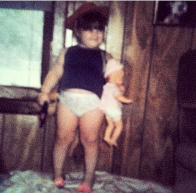 Blurry photo of a toddler holding a doll and wearing a brimmed hat