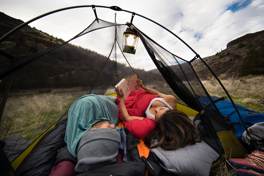 a couple laying in a mesh tent in what looks like a park 