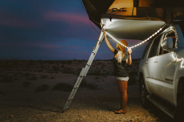 person stringing up the light string beside of a truck for camping