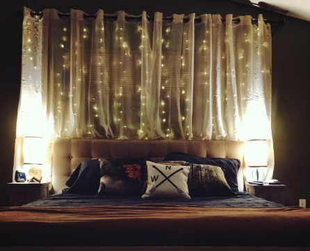 a reviewer&#x27;s photo of the twinkle lights hanging behind their bed