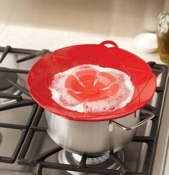 The spill stopper in red on top of a pot on a stove with water boiling inside, illustrating that it will not boil over