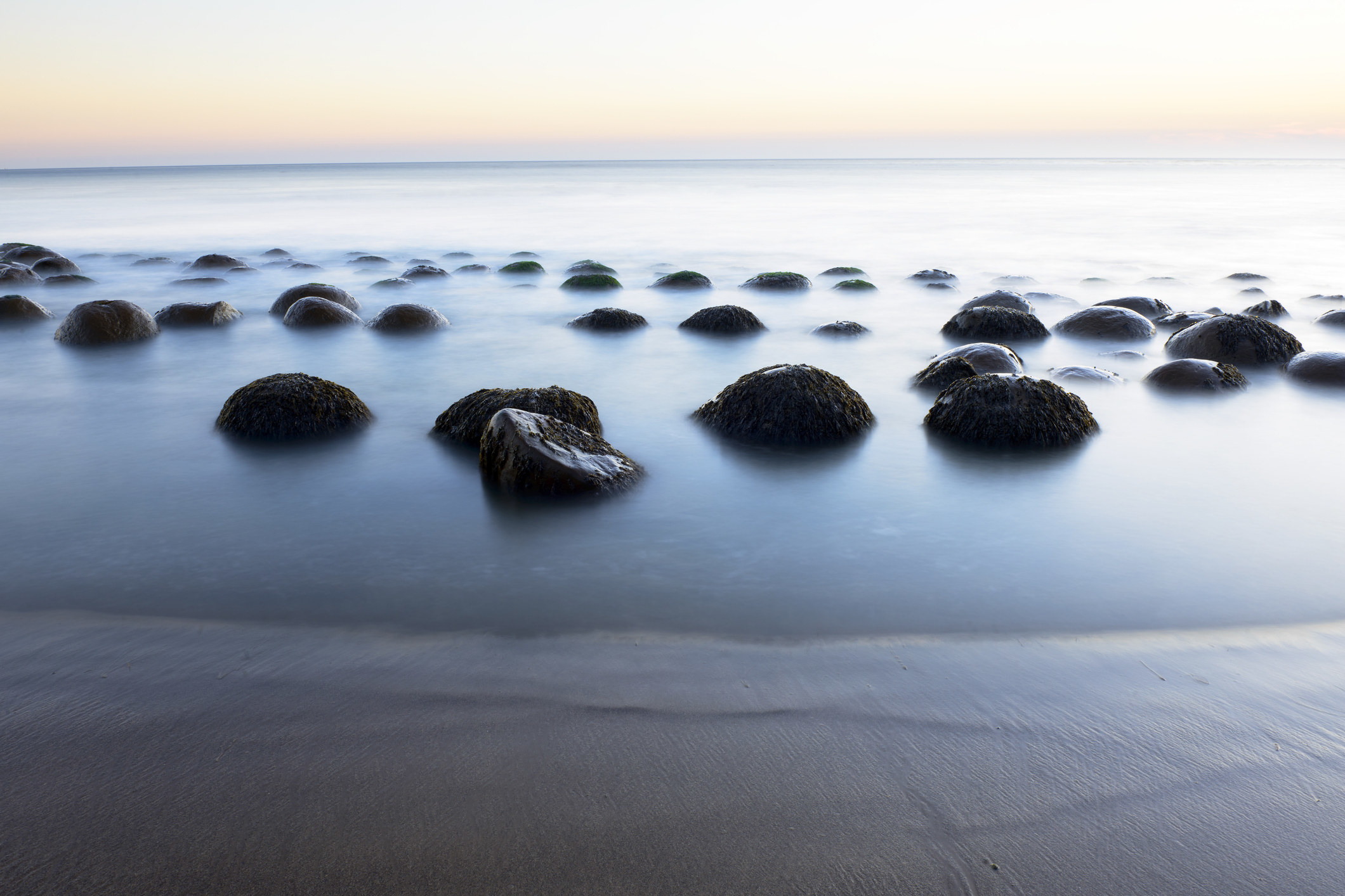 A serene beach setting with smooth rocks like bowling balls. 