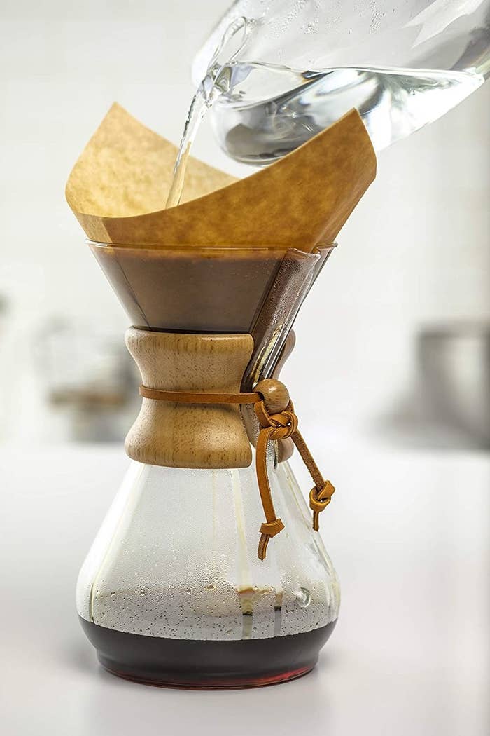 Someone pouring water in the glass coffee maker which has a wooden cuff