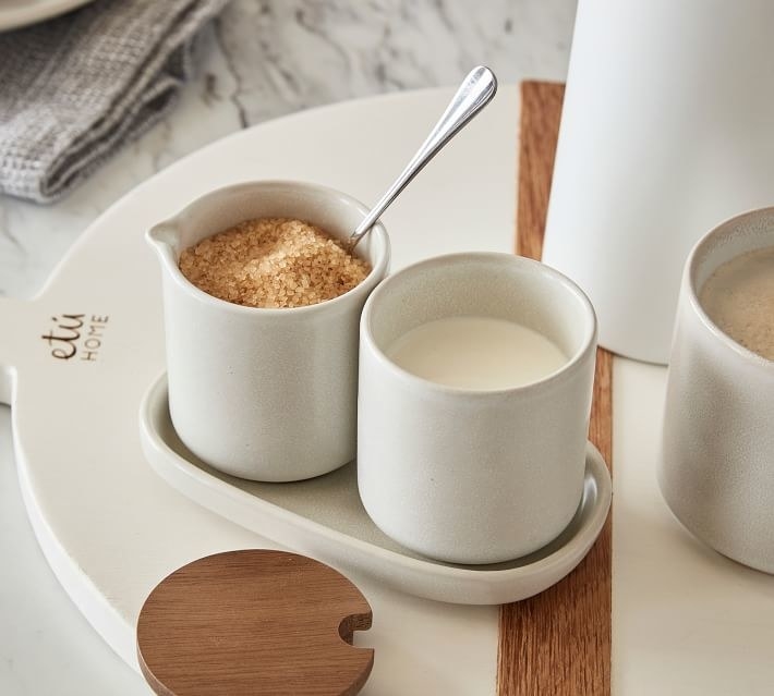 the white canisters holding sugar and cream and sitting on a stoneware tray