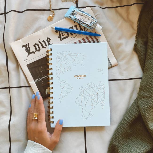 Model holding spiral notebook with minimalist gold map that says 