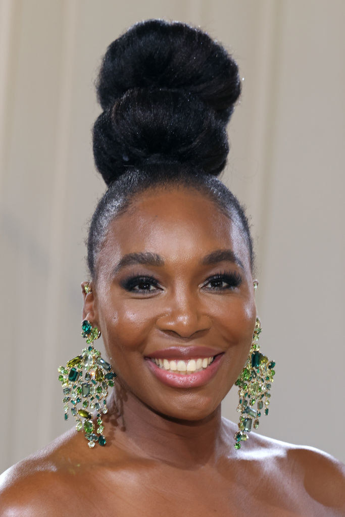A close up of Venus Williams as she shows off her dark eye makeup and high bun hairstyle