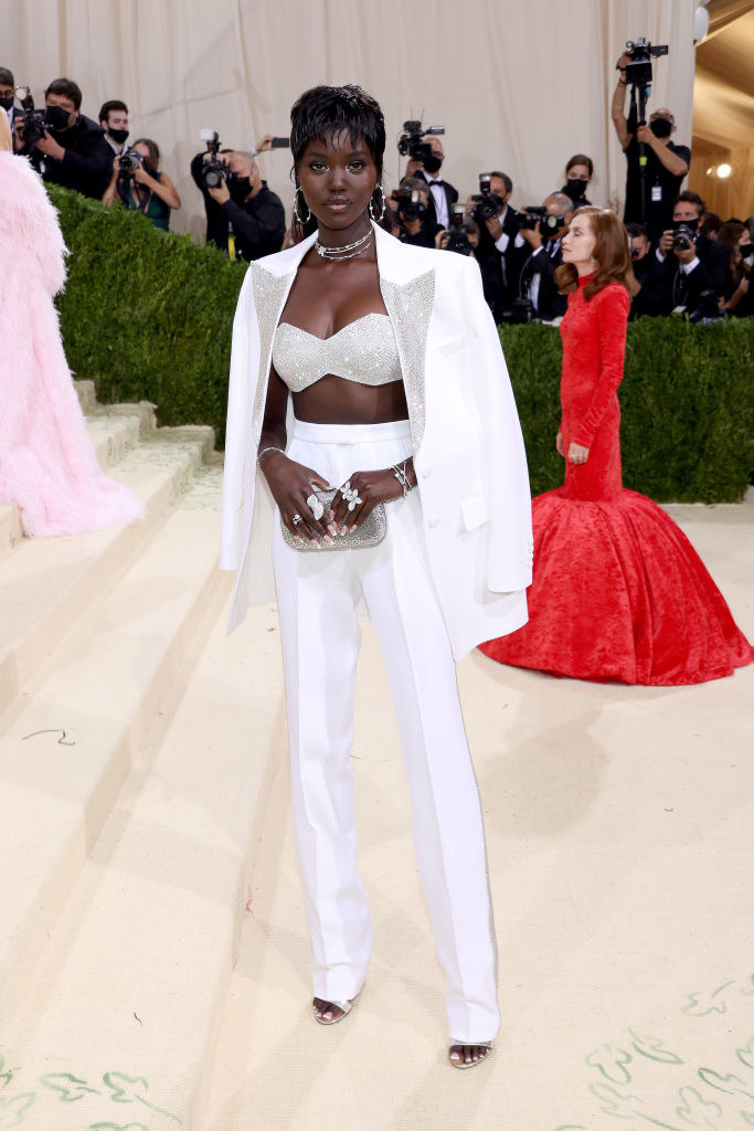 Adut Akech wears a sparkly bandeau and light colored slacks with a matching blazer