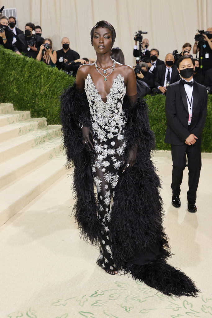 Anok Yai wears a dark gown with crystal patterns on it under a floor length fuzzy coat