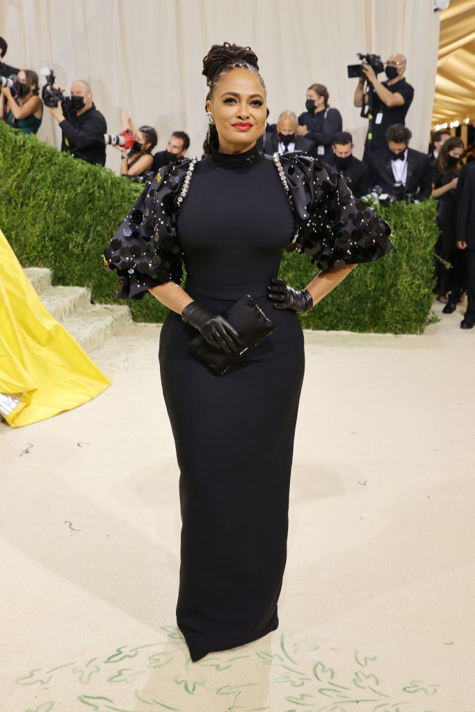 Ava DuVernay wears a dark puffy sleeve floor length gown and matching gloves