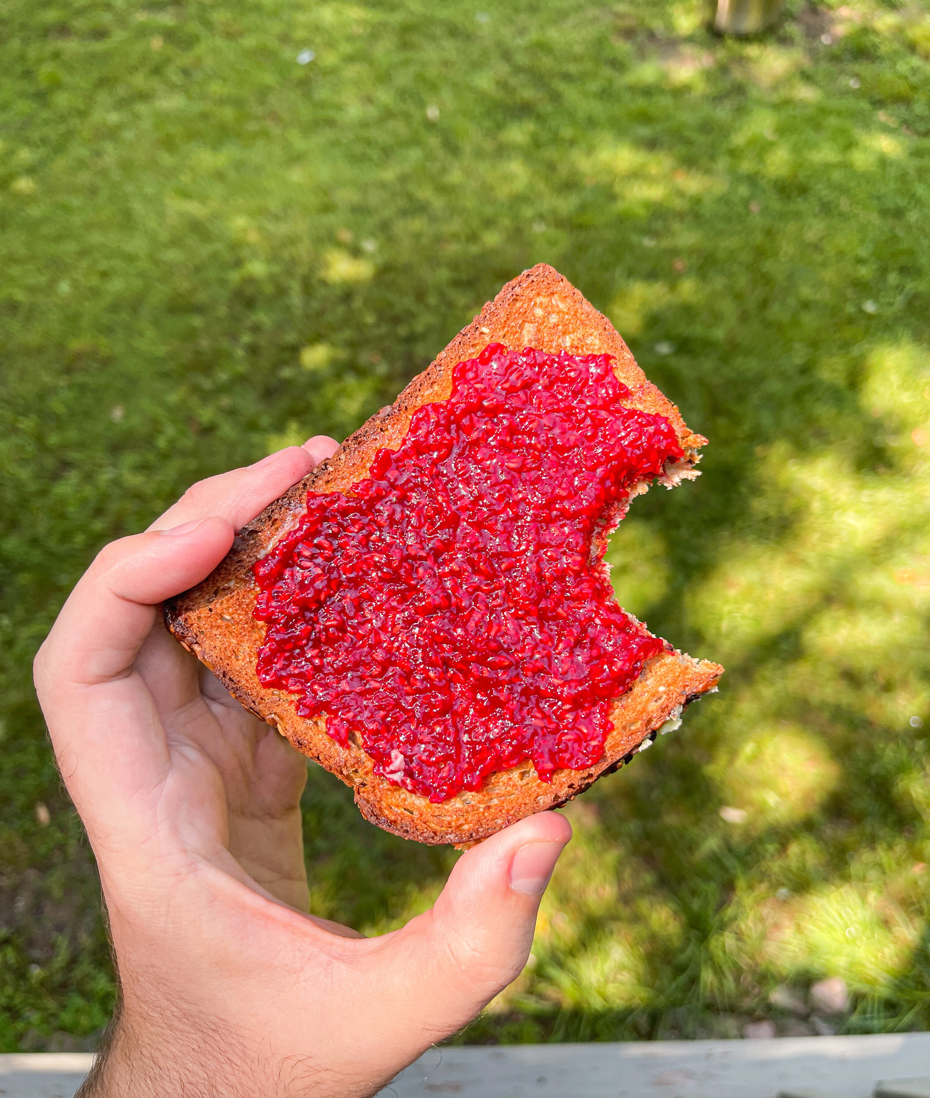 Raspberry jam spread on a bitten piece of toast