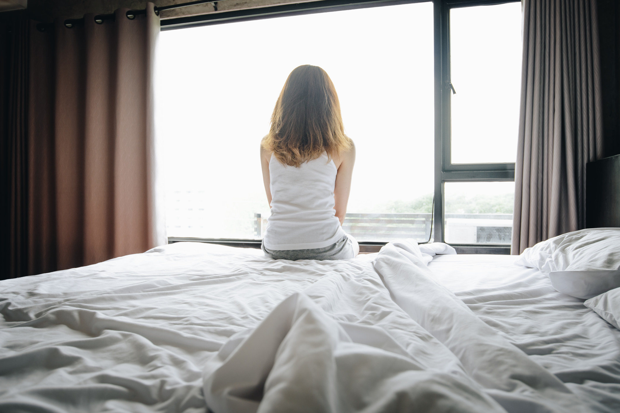 sad, lonely woman sitting on a bed looking out a window