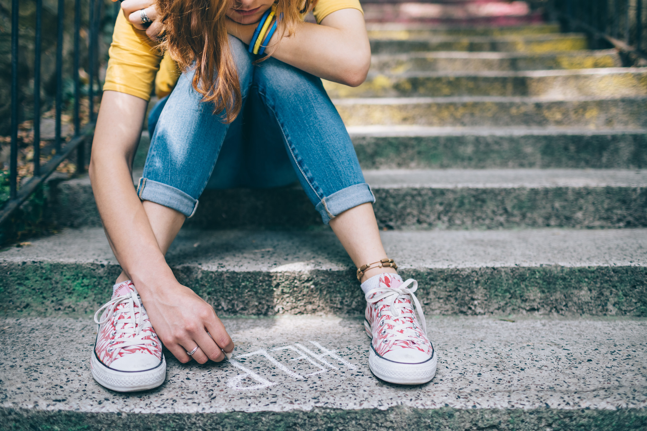 teen girl sadly sitting and writing &quot;help&quot; in chalk on the ground