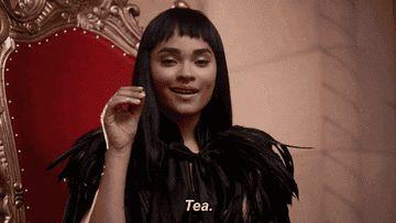 A close-up of a young woman as she puts her pinky out and says, &quot;Tea&quot;