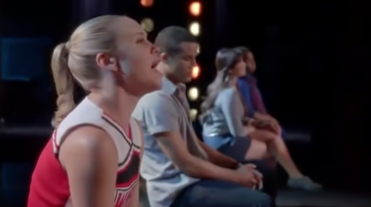 A close up of Kitty Wilde as she sings while sitting next to three of her classmates