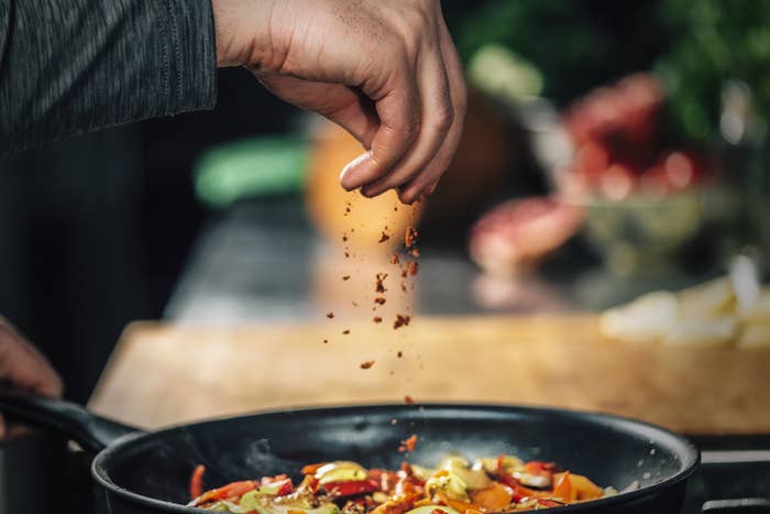 Someone putting spices into a skillet.