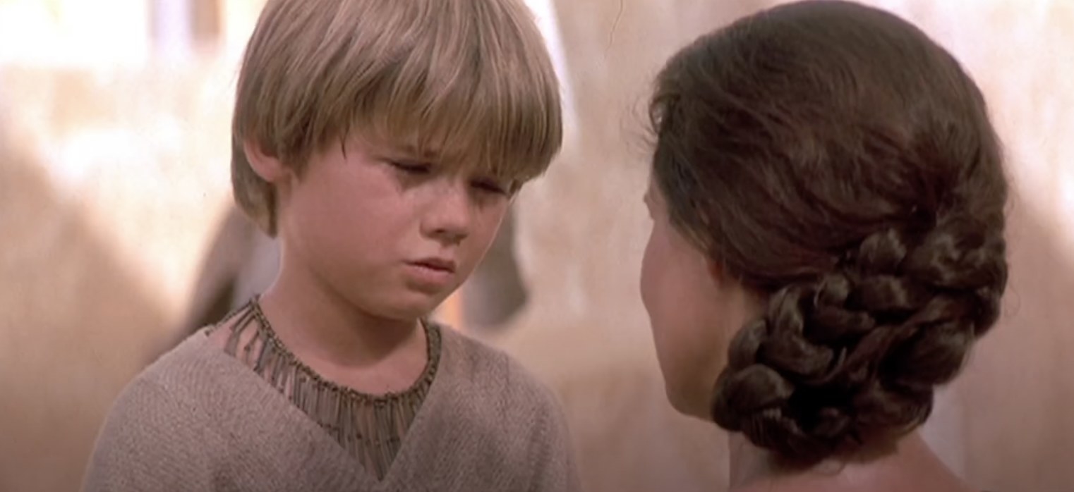 Anakin Skywalker, a young boy, faces Shmi Skywalker, a woman with braided hair, in a scene from a movie