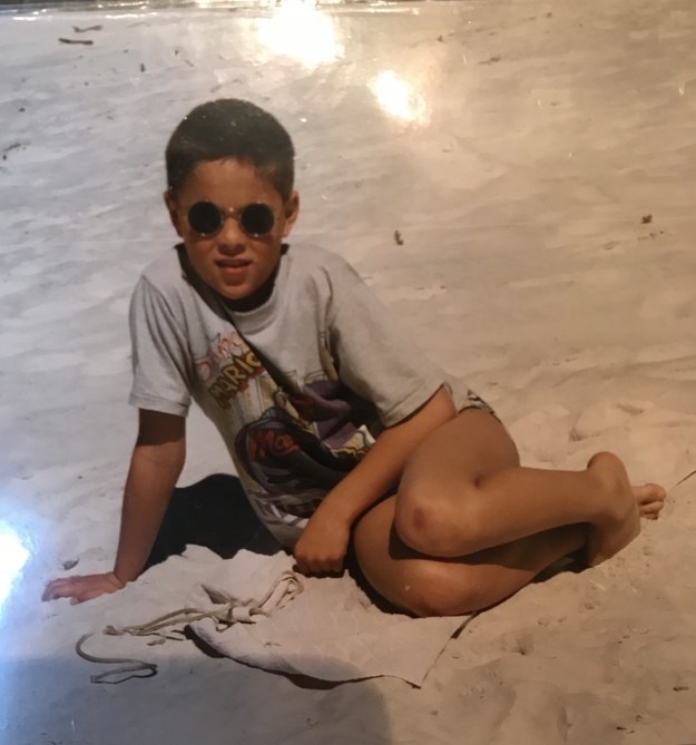 A child in a T-shirt and sunglasses sitting on the sand
