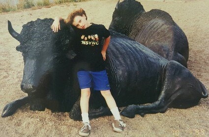 A young girl wearing an &#x27;NSYNC T-shirt and shorts and kneeling against a large bull statue