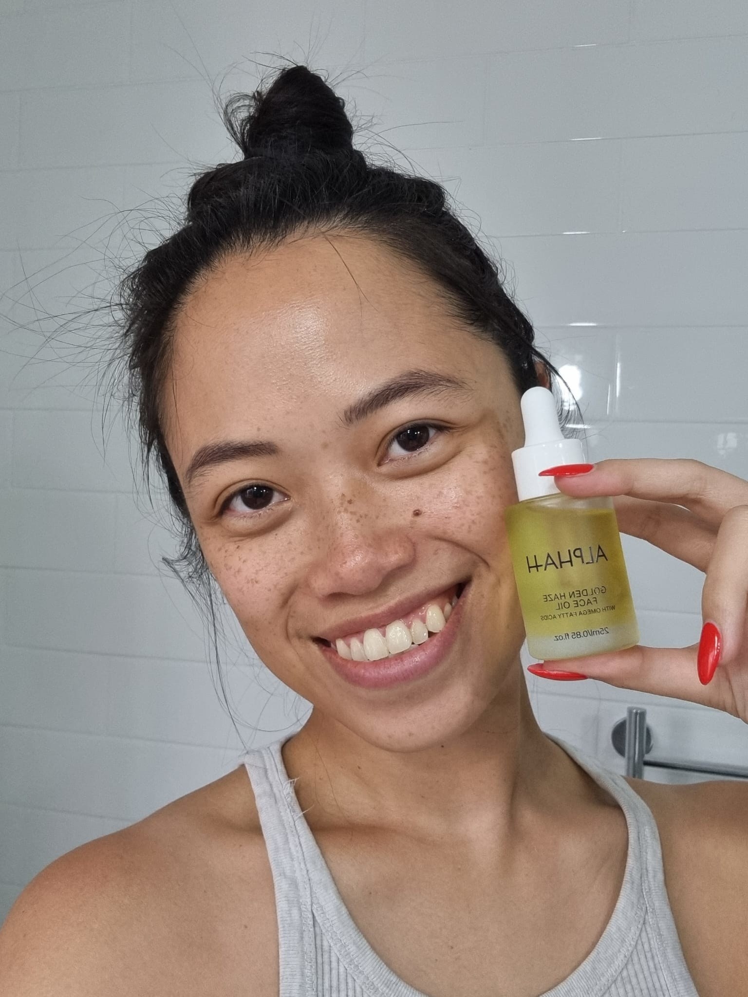 A woman holds a small bottle with yellow liquid in it to her face.