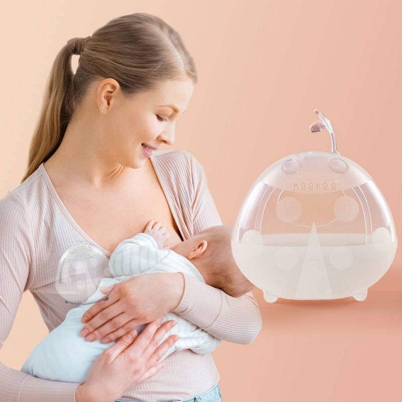 A person is using a silicone manual breast pump while holding a baby