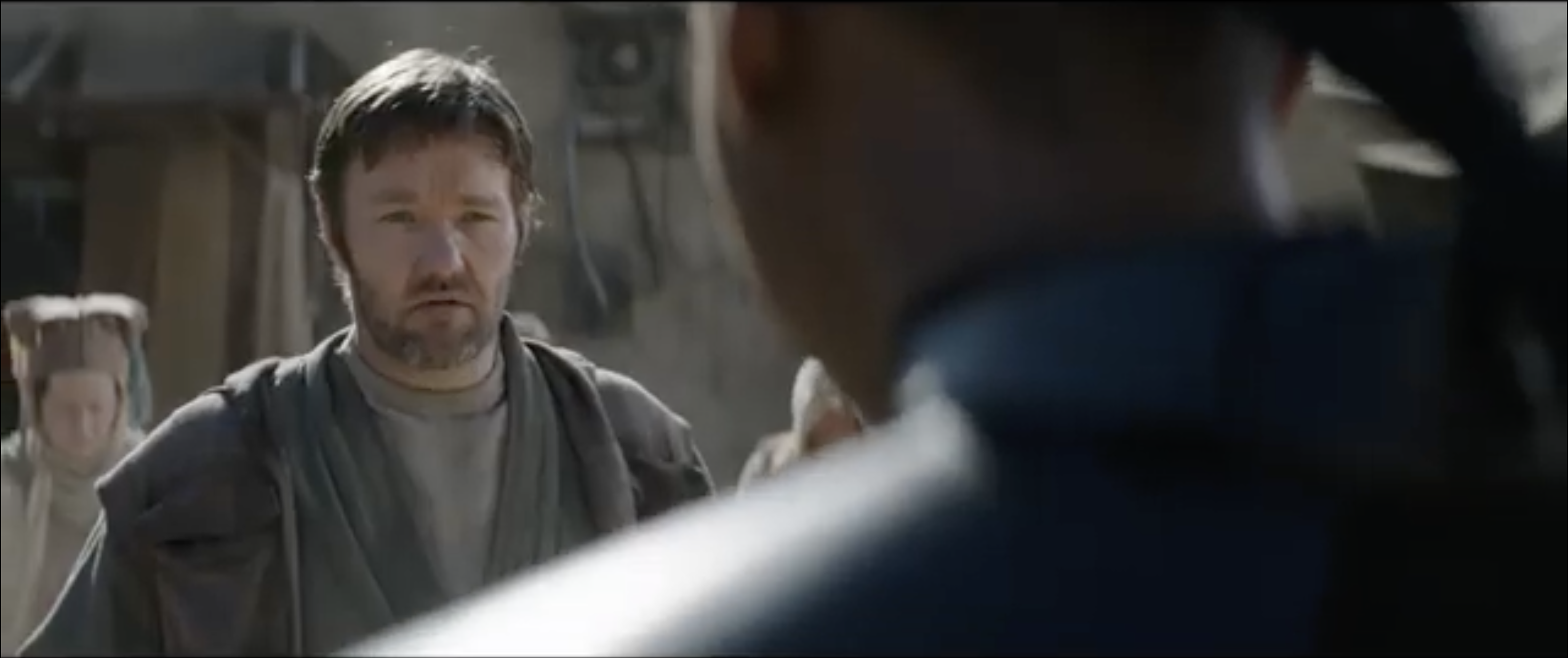 Joel Edgerton, dressed in rugged attire, faces a person with their back turned, in a scene from a television show or movie