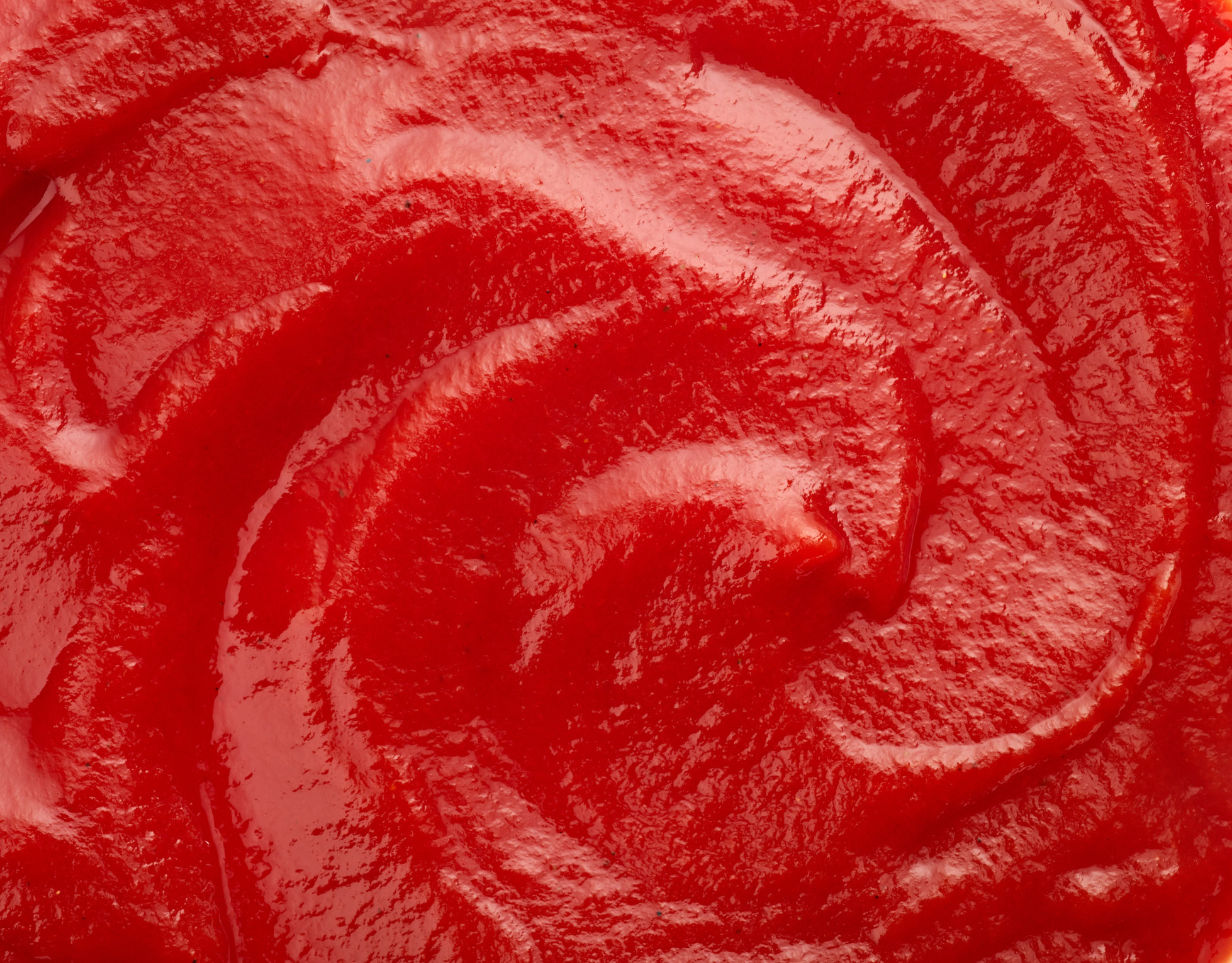 Close-up of a textured, red, swirling sauce, resembling the consistency of ketchup. No people or text present