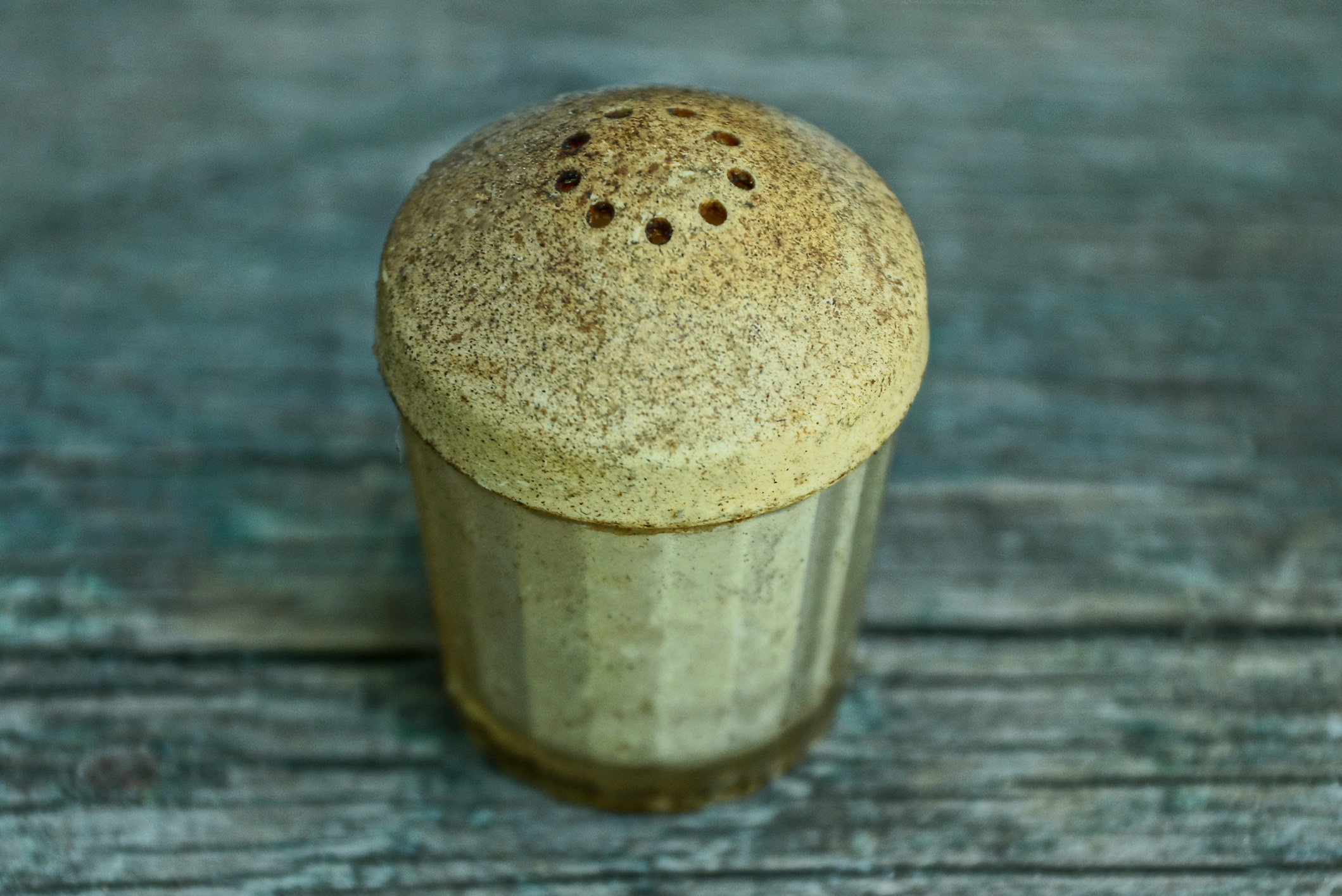 Close-up of a rustic, vintage salt shaker with a metal lid, placed on a textured wooden surface
