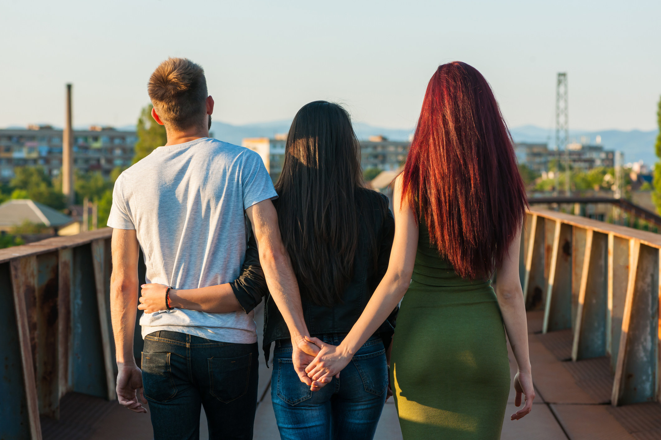 Woman and man holding hands behind another woman&#x27;s back