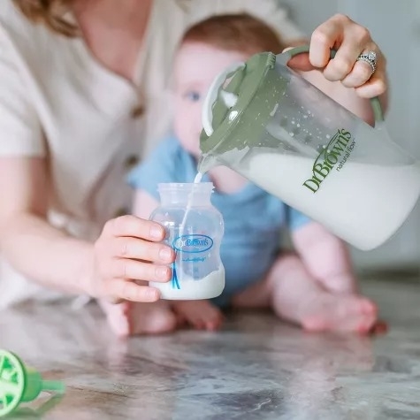 An adult fills a bottle with the mixing pitcher