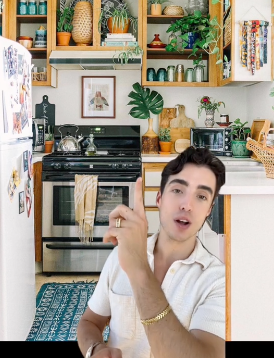 Tommy points to various layered elements in a kitchen with plants, open cabinets, artwork, etc.