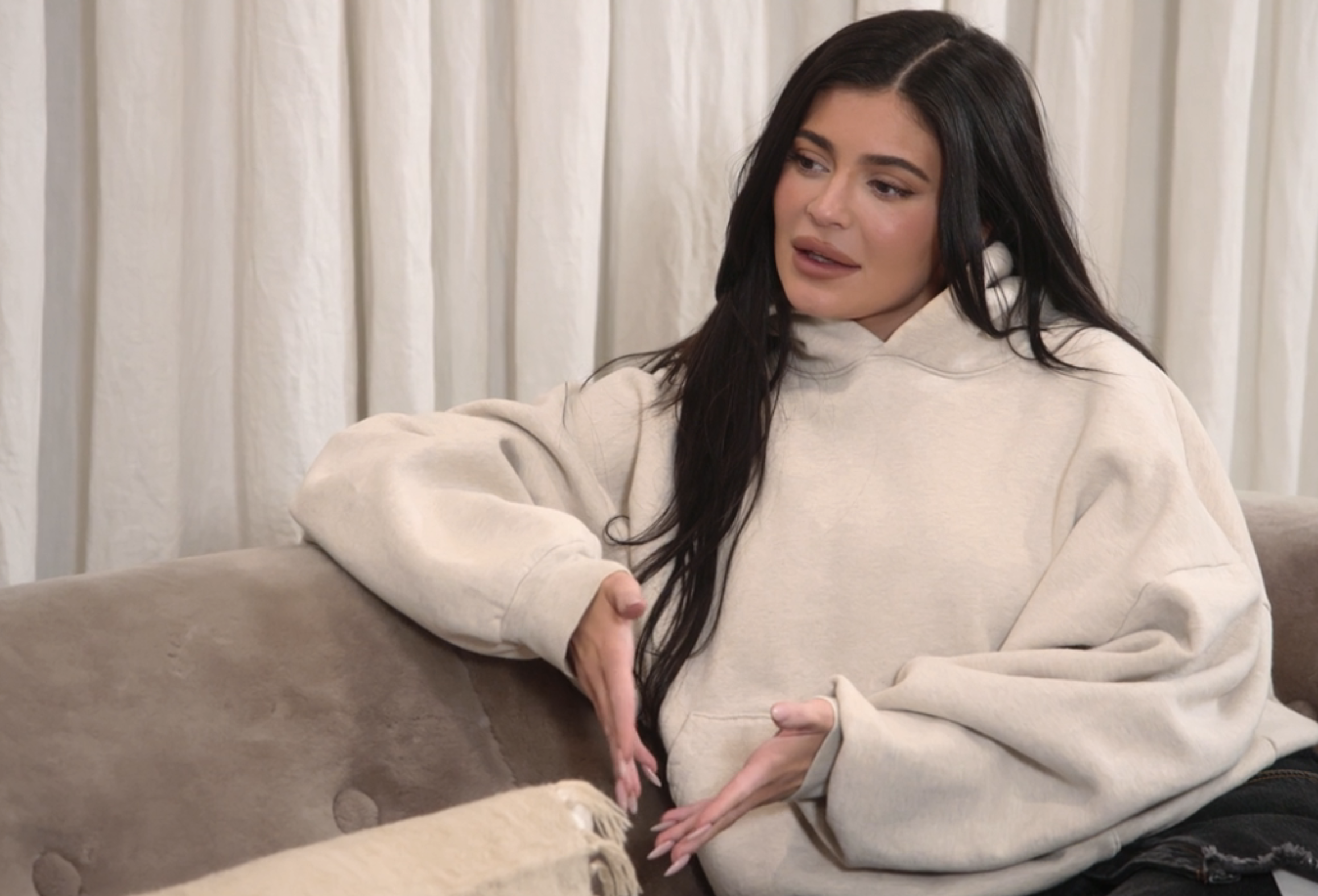 Close-up of Kylie sitting on a couch and wearing an oversize, long-sleeved hoodie