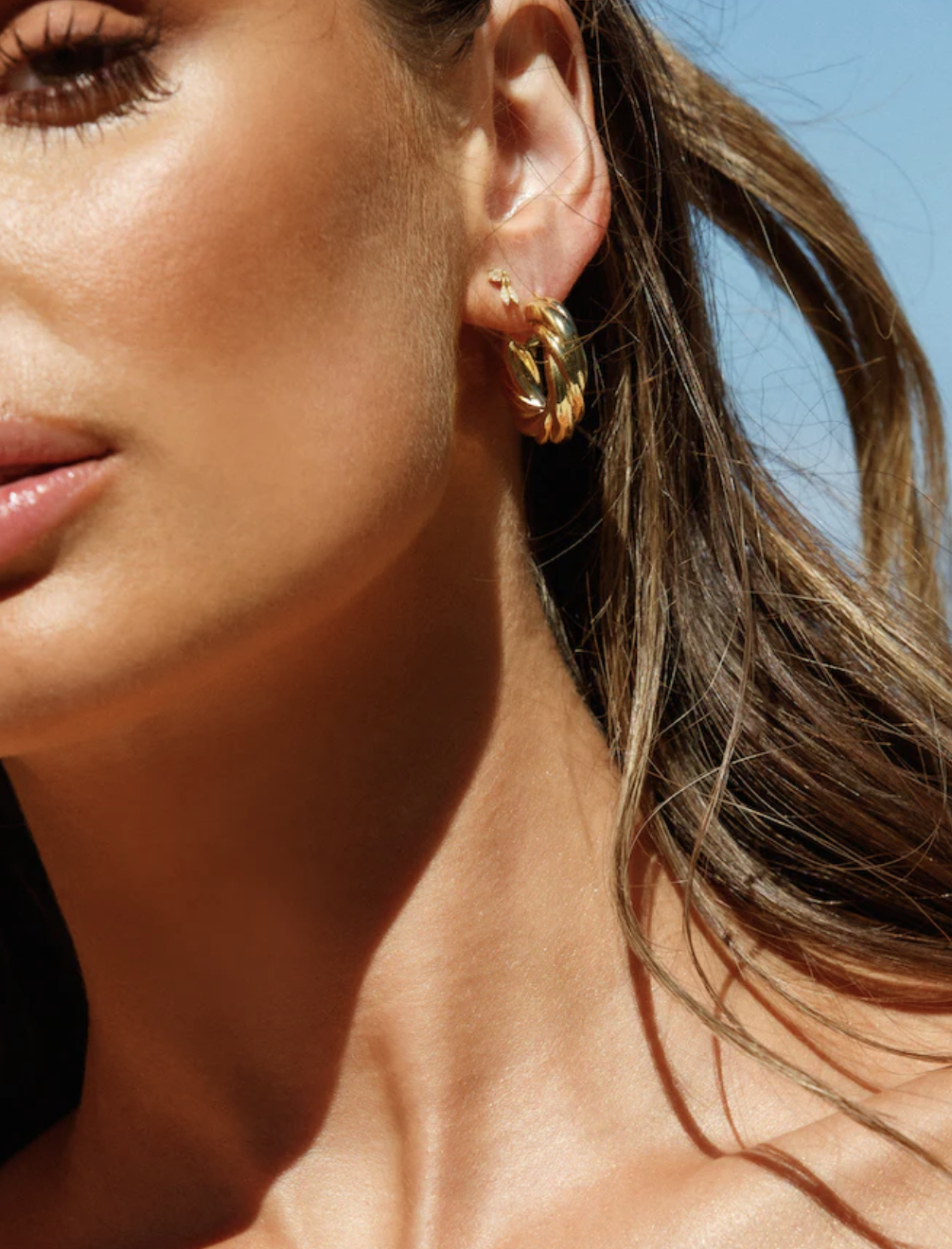 Close-up of a person wearing a hoop earring, focusing on the ear, cheek, and hair