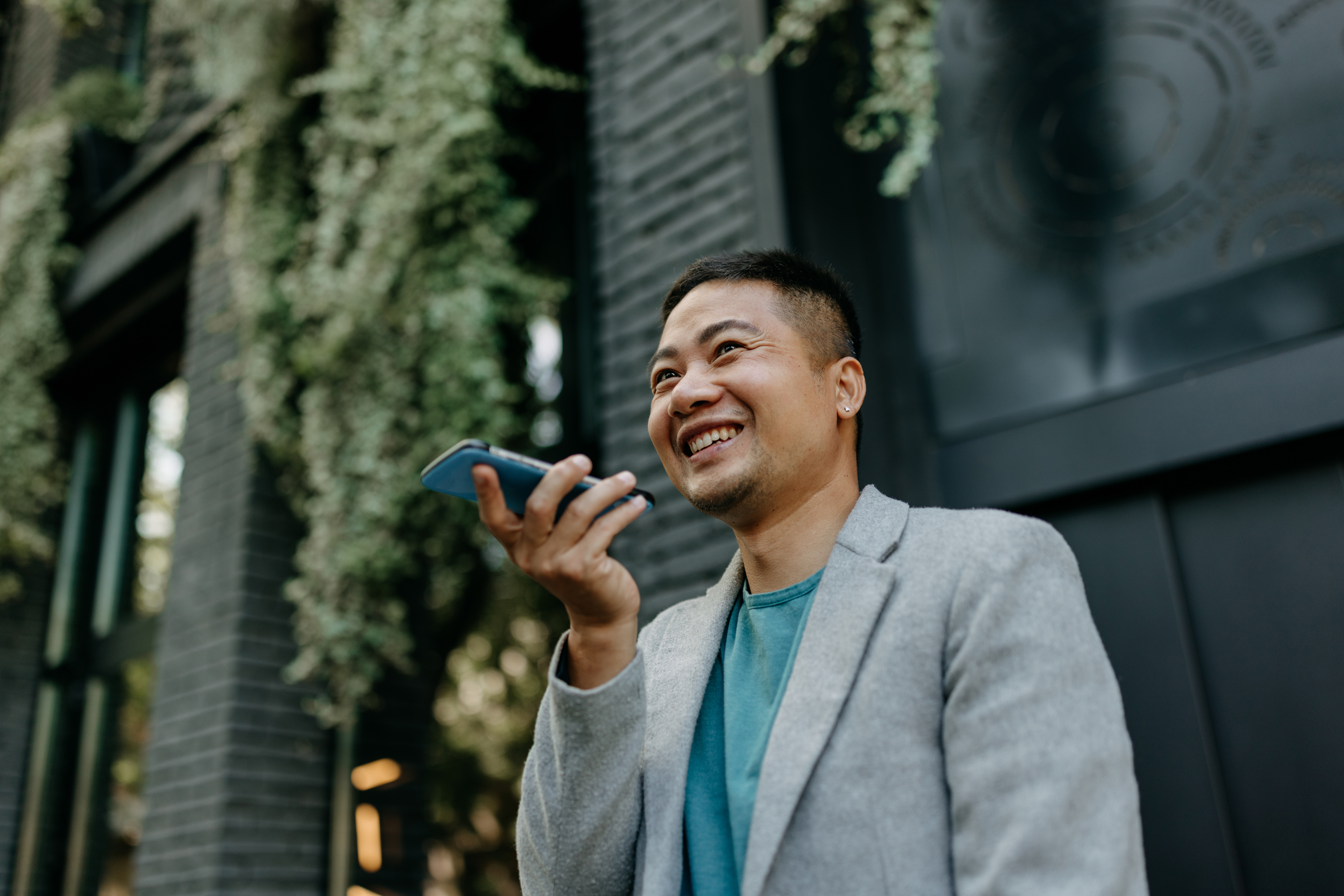 Man in a blazer holding a smartphone, smiling and looking away as if in a conversation