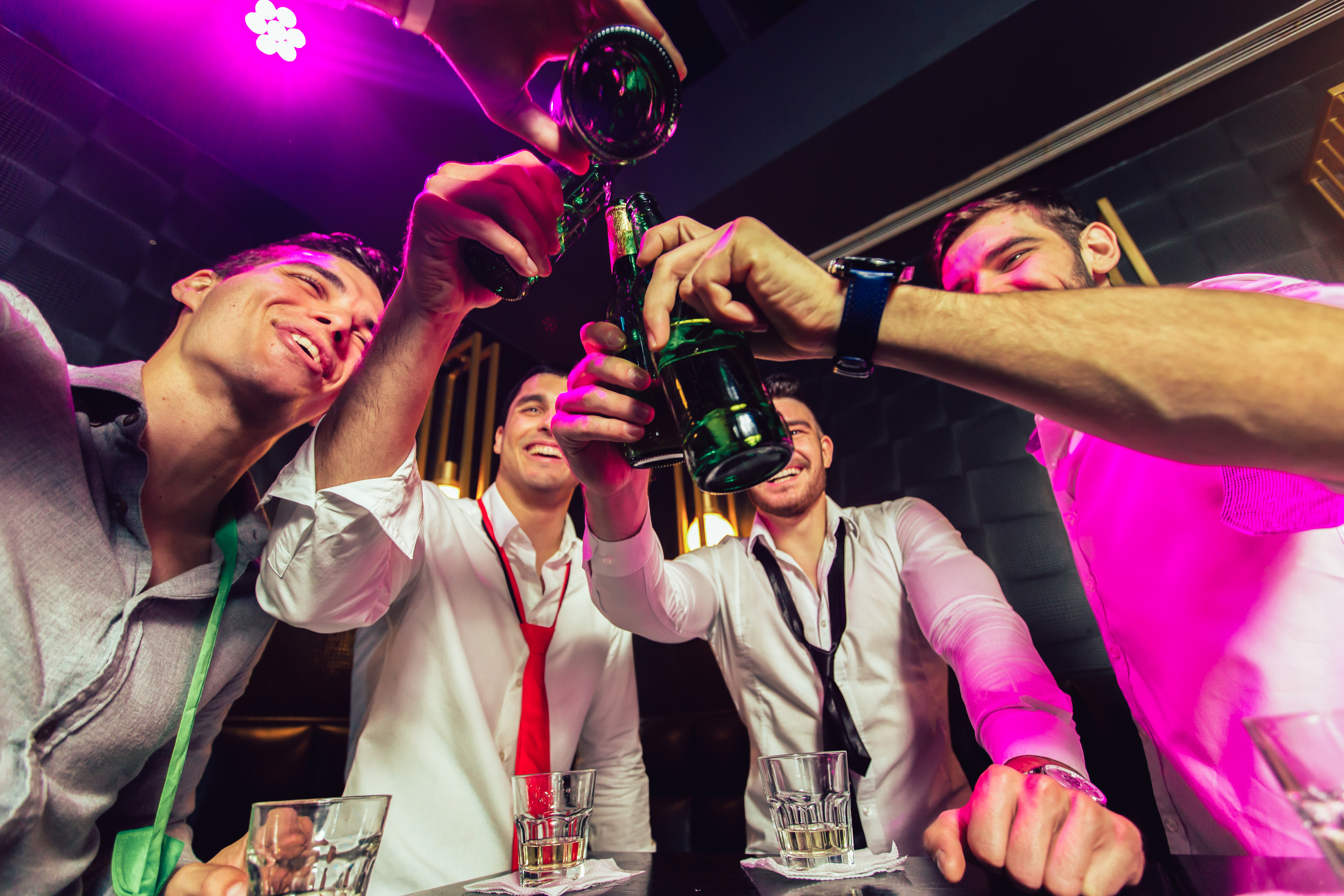 Group of cheerful friends toasting with small glasses in a dimly lit setting