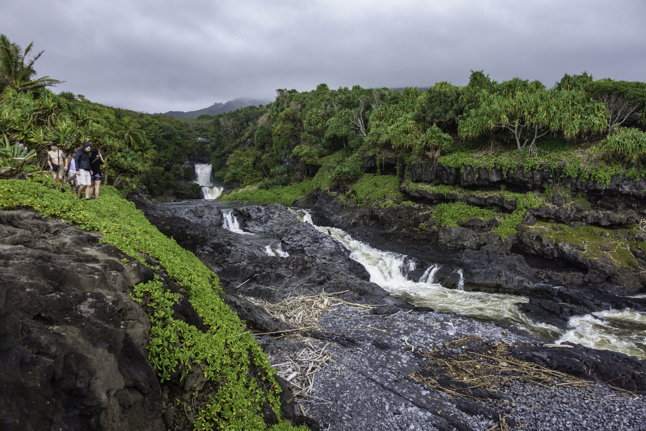 Visitors beside a rocky stream with a waterfall in a lush landscape