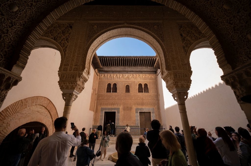 Group of people under an ornate archway, looking toward a building&#x27;s intricate facade